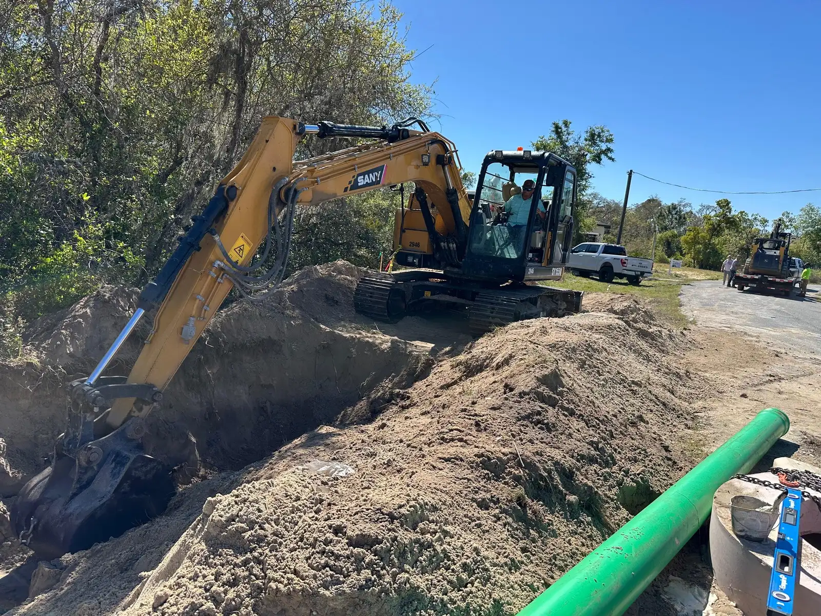 Excavator opening a utility trench in Florida with sewer pipe staged alongside