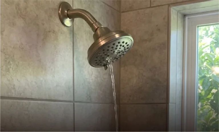 Shower head running with a weak, broken stream from low water pressure in a Florida home.